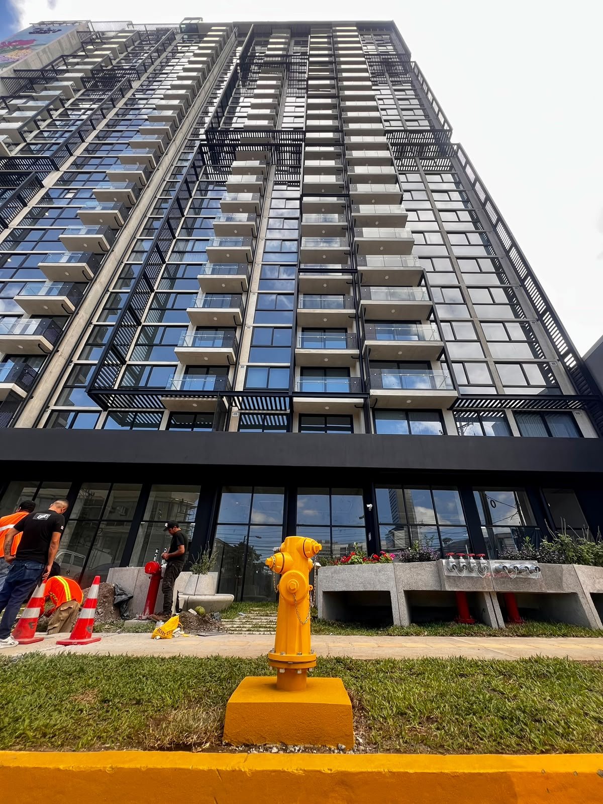 Yellow hydrant installed in front of a building, with field workers in the background